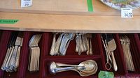 Red velvet-lined cutlery tray with a collection of silver plated flatware including knives, forks, spoons, serving spoon and tongs, organized by type.