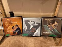 Three framed Frank Sinatra vinyl albums displayed on the floor leaning against a wall. Visible are the album covers for 'Songs for Swingin' Lovers!', 'Nice 'n' Easy', and 'Where Are You?'.