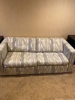 Front view of the sofa bed couch showing geometric patterned upholstery in beige, gray and cream colors with a boxy frame and armrests.