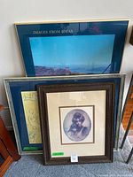 Photo of three framed artworks leaning against a wall, highlighting the Val Miller framed mother and child piece at the front.