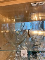 Large clear glass salad bowl and glass vase on a wooden shelf inside a cabinet.