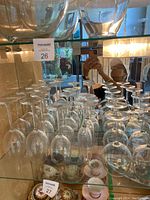 Assorted wine glasses placed upside down on glass shelves inside a cabinet, showing varied shapes and clear glass material.