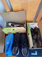 Four pairs of women's shoes size 8.5 displayed with some in shoeboxes. Blue water shoes, black sneakers, and two different sandals.
