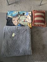 Three items shown together: Avatar the Last Airbender throw blanket folded with characters visible, grey throw blanket folded with tag, and rectangular striped cushion with fringe trim