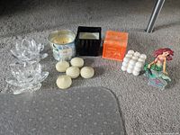 A group photo showing all items including the Ariel figurine, two clear lotus tea light holders, six white tea light candles, one jar candle, one black square candle holder with candle, and one cluster white pillar candle.