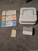 Overall view of the robotic mop, charger, and three unopened cleaning pads in different colors and functions.