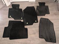 Six floor mats for Mazda3 vehicle including four black carpet mats and two molded rubber mats with Mazda3 branding arranged on floor.