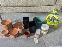 Full lot showing ceramic saucers stacked in piles, black square plastic pots, green round plastic pot, small orange plastic pot, fertilizer container, and orchid potting mix bag.