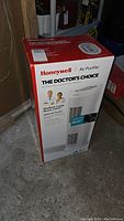 Boxed Honeywell air purifier unit standing on floor showing front of packaging with product image, brand and model number information.