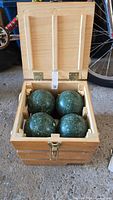 Wooden box open showing four green bocce balls inside.