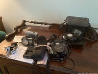 Photo showing three cameras: Fujifilm FinePix F200EXR, Mamiya-16, and Olympus C-5060 along with charger, manual, flash, and carrying cases spread on a wooden table.