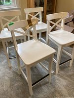 Four white wooden nook chairs with cross-back design arranged together, showing overall shape and style.