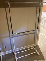 Full front view of the clothes rack against a beige wall and wooden flooring.