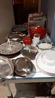Cookware and serveware including red Le Creuset roaster, metal pans, white ceramic bowl, candy dishes, and servers on a table.