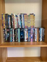 Front view of multiple DVD and Blu-ray titles neatly arranged on wooden shelf showing a mix of TV series and movies.