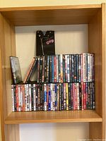 Full view of DVD shelf showing various DVD titles stacked in three rows and a large Grease-themed DVD case on top.