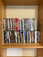 Front view of DVDs arranged on wooden shelf, showing front cover artwork and titles of various movies.