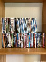 Front view of DVD collection arranged on a wooden shelf, showing multiple rows of DVD cases with visible spines and titles.