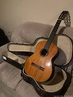 Full view of Fender Classic FC-10 acoustic guitar resting in open hard case on a couch, showing overall condition and case lining.