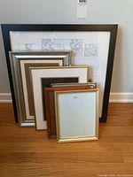 Grouped view of eight assorted picture frames in various sizes and styles against a wall.