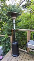 Full view of outdoor propane patio heater standing on wooden deck with trees in background.