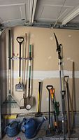 Full view of garden tools hanging on wall including rakes, shovels, edger, sledgehammer