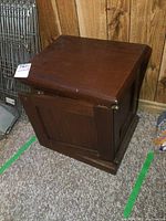 Front angle view of the antique wooden filing cabinet showing one visible drawer panel and brass corner caps on the top edges.