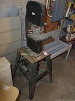 Band saw mounted on metal stand with visible belt drive motor and enclosed blade covers.