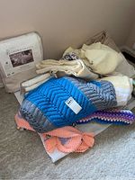 Photo showing the packaged Crown Crafts quilted Matelassé bedspread and several assorted blankets including crocheted and other types.