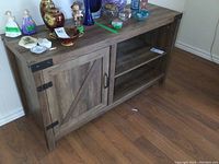 Full view of the wooden cabinet showing barn door style door on the left and two shelves on the right with items on top.