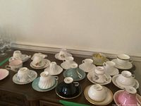 Wide view of 11 assorted porcelain cups and saucers on wooden table, some upside down showing bases