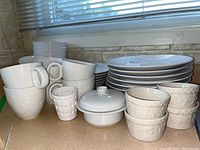 Side view of stacked bowls, mugs, dinner and lunch plates, and butter dish with lid