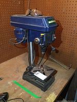 Mastercraft bench top drill press on wooden workbench showing side profile with safety glasses on top.