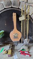 Photo showing fireplace tool set on stand, vintage bellows with brass ship decoration, matches and lighters arranged at base, set against stone fireplace.