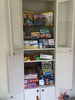Full view of cabinet with multiple shelves filled with boxed games and puzzles including Roll O Puzzle, various 1000 piece puzzles, and other boxed board games and toys.