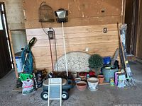 Full lot view showing hanging birdcage, garden wagon, large cherub wall decor, gardening pots, bags of potting mix, and garden tools.