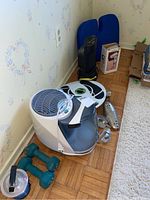 Photo showing Sunbeam humidifier front and side with control dials, Revitive foot massager behind, metal shoe stretchers, small lantern, two blue 5 lb dumbbells on floor next to humidifier.