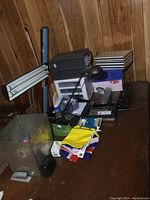 Desk surface view showing two desk lamps, stacked organizers, various punches, tape dispenser, staplers, stationary papers, and boxes.