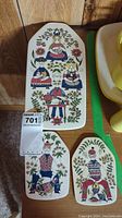 Full view of the set of three hand-painted ceramic tiles showing detailed folk art human figures and flower designs on wood surface.