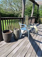 Overall patio set on wooden deck with webbed gravity chair, white resin plastic chair, and two planters of woven and resin bark style.