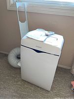 Front and side views of the white Noma portable air conditioning unit with remote and venting hose attached.