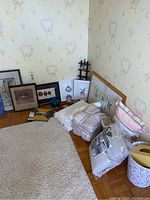 Overview of framed prints, bedding items including throws, duvet cover, drapes, and other home decor items on floor against wall