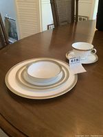 Full place setting stacked showing cup and saucer, fruit nappie, bread and butter plate, luncheon plate, and dinner plate with MaxSold tag number 619.