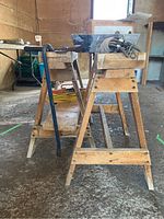 Pair of wooden sawhorses shown from front angle inside a garage, with a crowbar leaning against one sawhorse and a coil of rope with pulley hooks placed on top of a sawhorse.