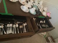 Top drawer showing diverse set of silverplate flatware with mixed patterns including forks, spoons, and serving utensils.