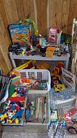Wide view showing plastic toy cars and trucks, large containers with LEGO bricks, children's books, and an Indian Chief sign leaning against the wall