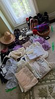 Full lot overview of women's sweaters, tops, shoes, hats, scarves and jewelry laid out on carpet