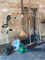 Full view of all yard tools and hand tools in the lot showcasing trimmer, blower, rake, broom, snow shovel, car brush, extension pole, and bucket with cord.