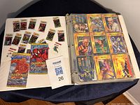 Photo showing the binder open to display 18 cards per page, colorful Marvel characters and Overpower game branding visible, with unopened booster packs included.
