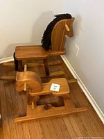Two wooden rocking horses placed on hardwood floor; one with yarn mane and the other smaller and simpler design.